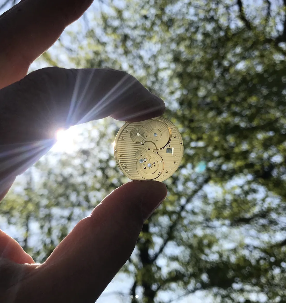 Un calibre FM01 tenu à contre-jour sous les arbres
